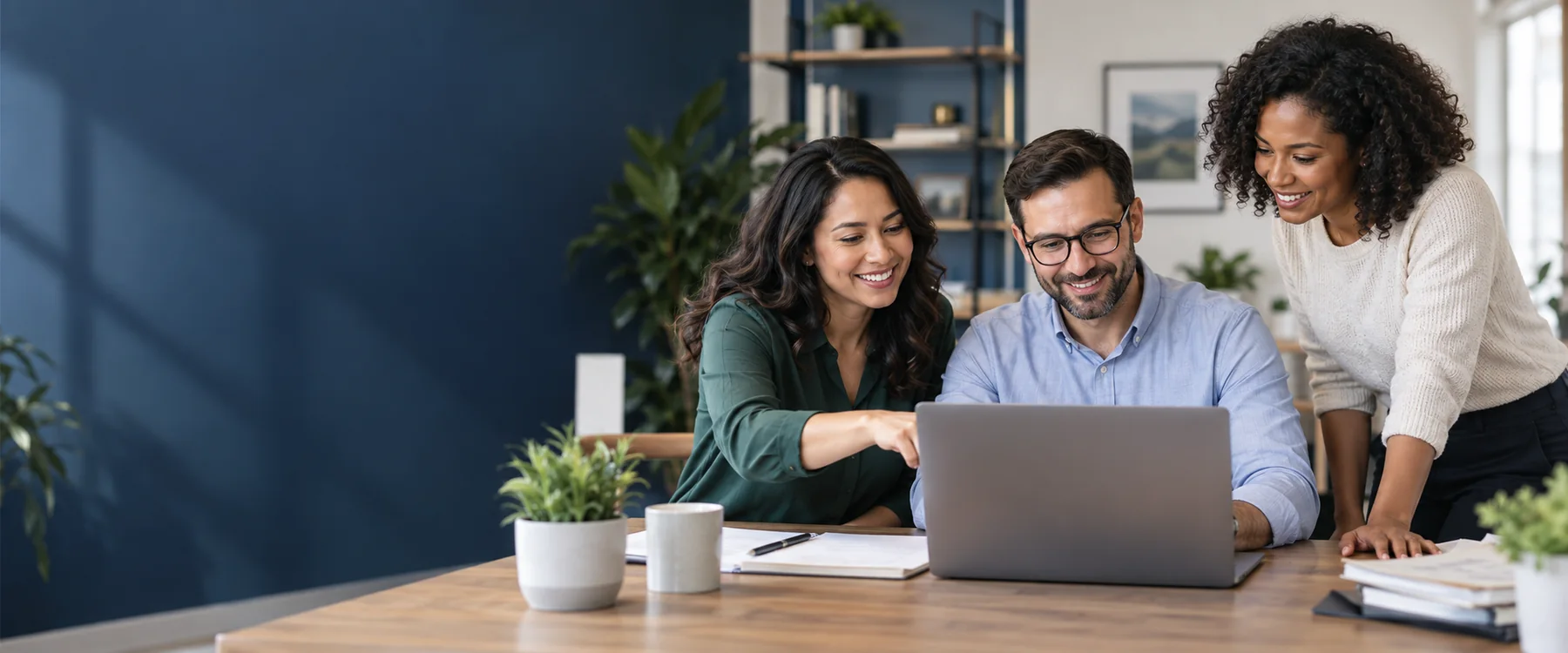 Illustrative photo of three professionals smiling and collaborating around a laptop.
